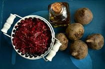 A bowl of red shredded beets, next to dirty whole beets on a blue table.