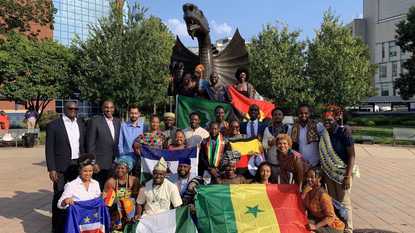 Two rows of people standing in front of the dragon statue on Drexel&#39;s campus holding flags of their home African countries.