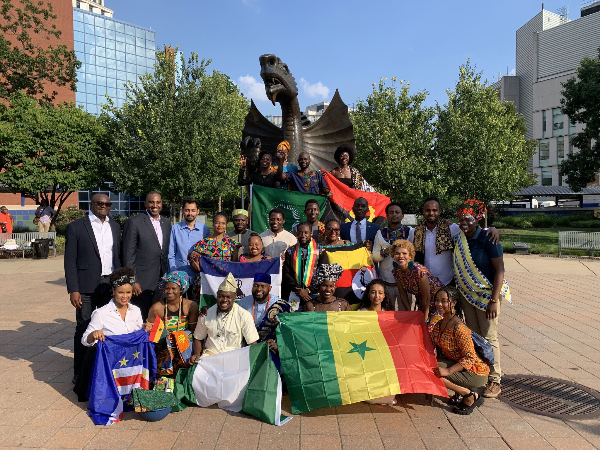 Two rows of people standing in front of the dragon statue on Drexel's campus holding flags of their home African countries.