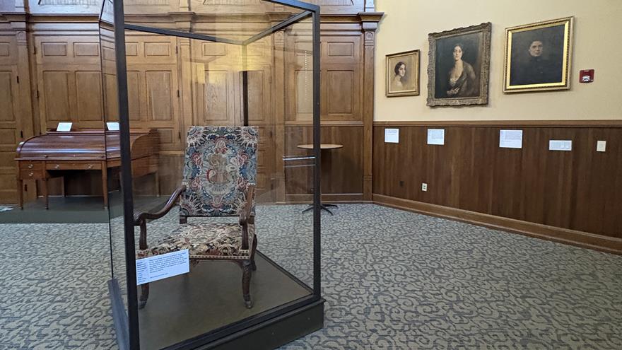 A view of a historical chair in a glass case in front of Drexel portraits.