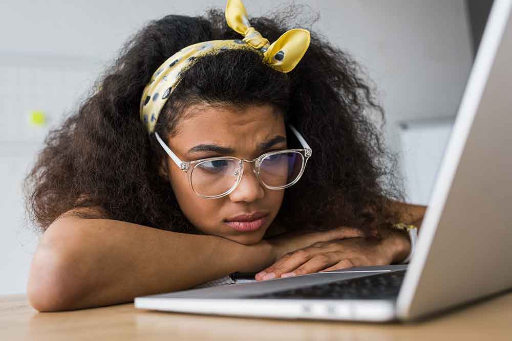 Stock photograph of teen appearing upset while using laptop computer