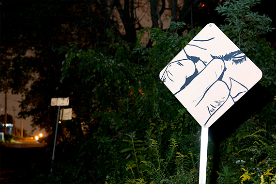 'In the Woods' by Nick Cassway, a diamond shaped traffic sign infront of a lush green space has a close up sketch of a person touching their face.