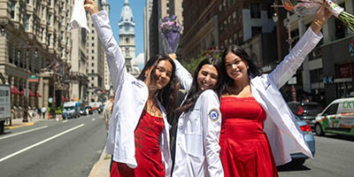 three students wearing their white coats with cars and buildings in the background